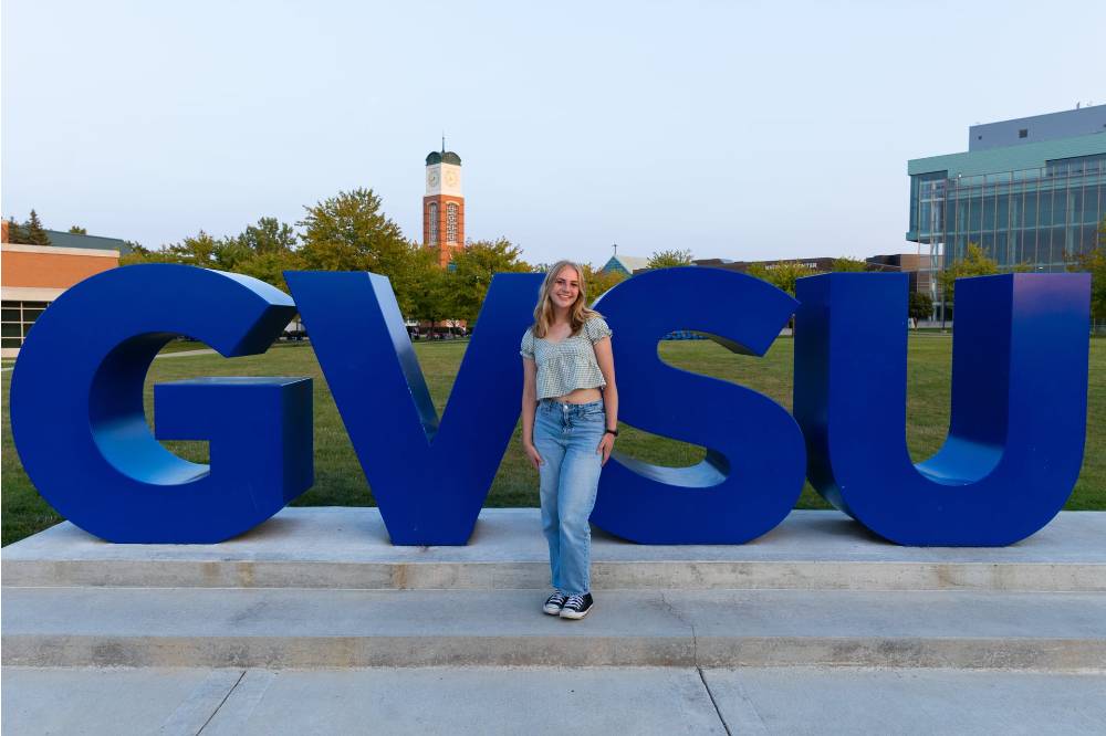 Image 1 of 2 Woman standing in front of GVSU lettering on Kirkhof Lawn, smiling